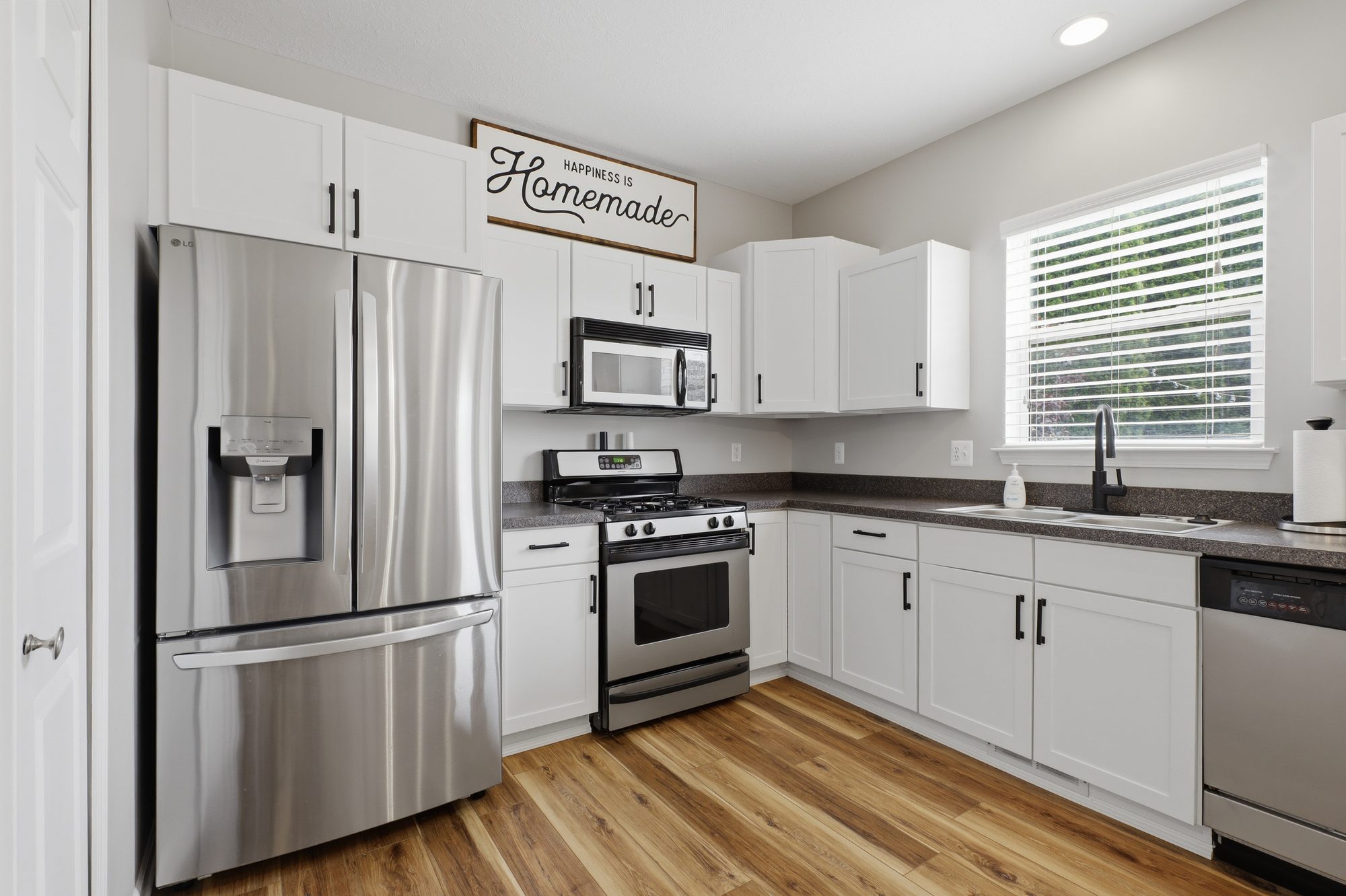 Professionally edited photo of a bright kitchen with white shaker cabinets, a stainless refrigerator, and a window over the sink